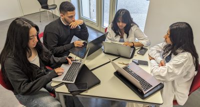 students sitting around table working on laptops
